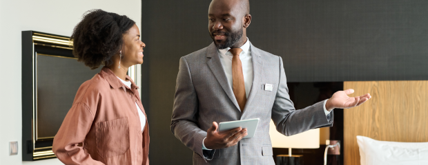 A hotelier with a tablet device shows a guest to her room.
