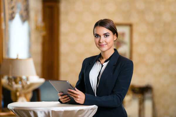 A smiling hotel agent ready to greet event guests with a tablet device in hand.