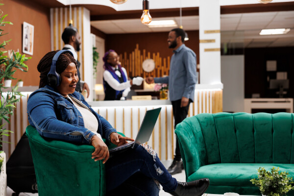 A smiling solo traveler with a laptop relaxes and works in a comfortable hotel lobby