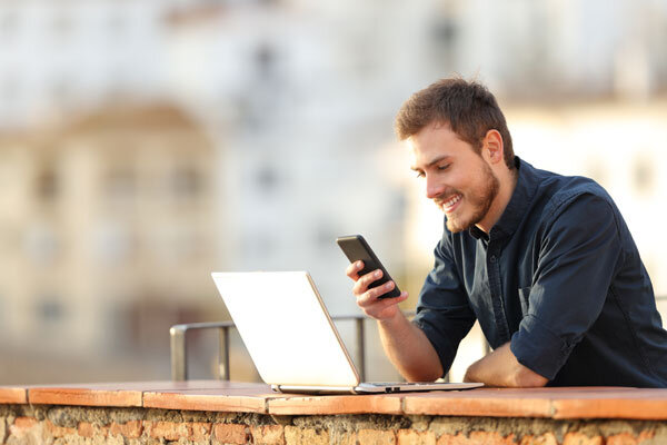 A traveler researching hotels online with both a smartphone and a laptop.