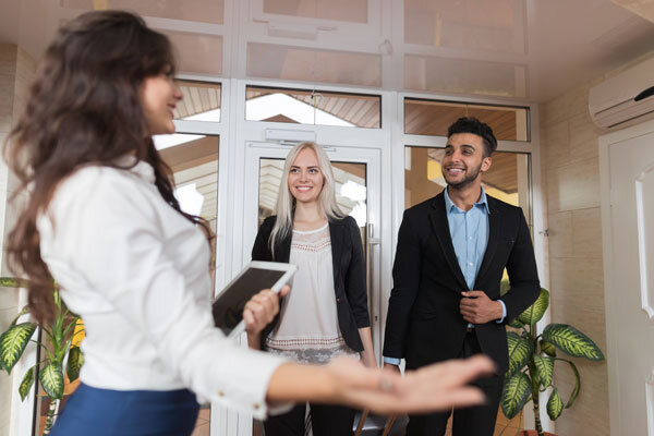 A smiling hotel employee with a tablet device in hand greets guests as soon as they arrive through the lobby door.