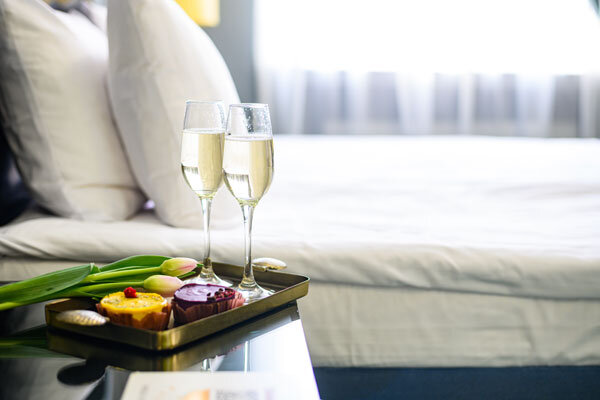 Two glasses of champagne on a tray with fresh cut flowers in a hotel room await guests celebrating their anniversary.