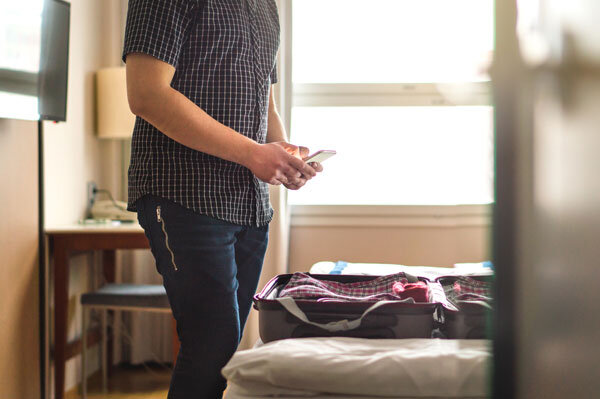 A guest packs his suitcase in his hotel room while using his mobile phone to complete contactless check out.