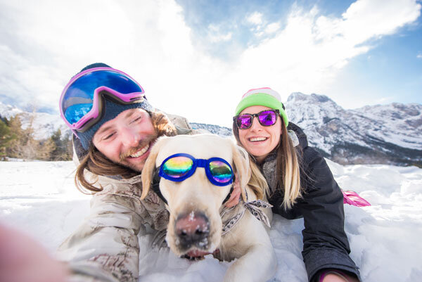 A couple takes a pet selfie with their labrador in the snow while on vacation