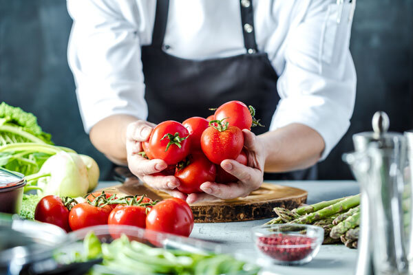 A chef prepares a meal with bright red organic tomatoes and other locally grown produce.