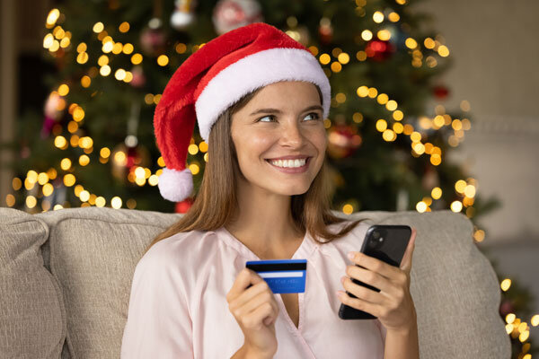 A smiling woman in a Santa hat buys a hotel gift certificate online with her mobile phone.