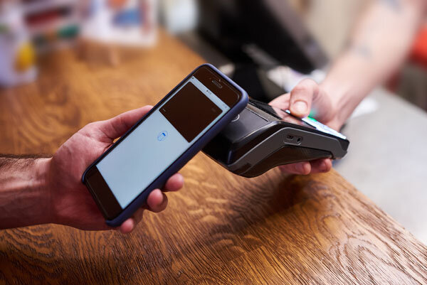 A man holds his mobile phone over a handheld payment terminal to make a convenient, contactless payment in a shop.
