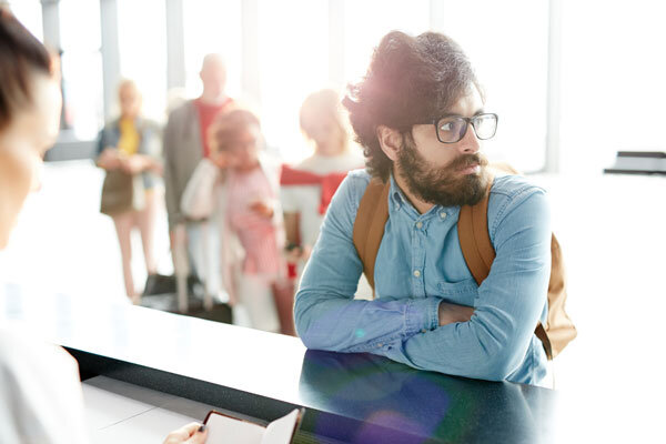 A tired guest waits at the front desk with more tired guests behind him.