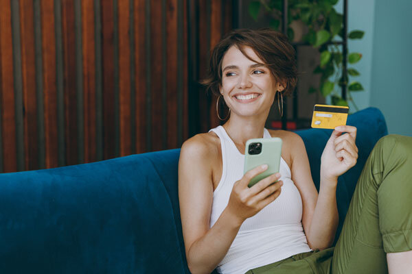 A smiling woman holding a credit card makes a hotel booking on her mobile.