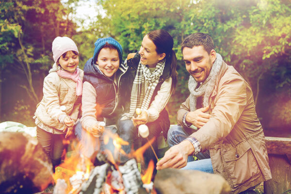 A family of four enjoys roasting marshmallows around a fire pit