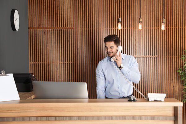 A smiling boutique hotel receptionist takes an appointment by phone and enters it into their reservation system.