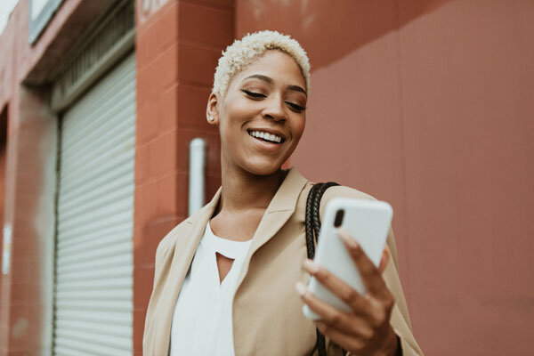 Image shows a smiling woman communicating with a chatbot on her mobile phone.