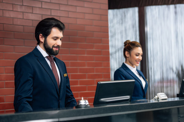 Two smiling hotel receptionists working with computers together at the front desk