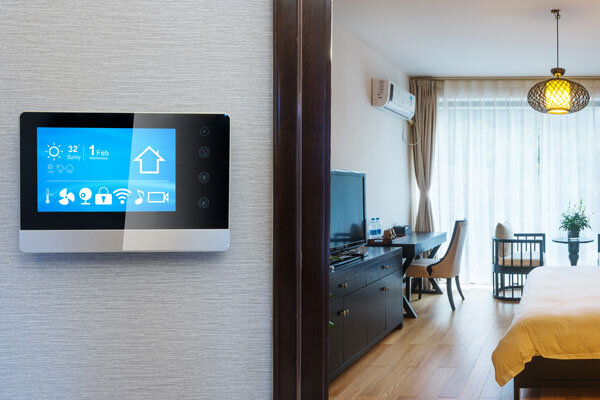 Image shows a wall-mounted smart room control panel with the guestroom in the background
