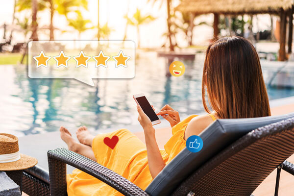 A hotel guest reclines by the pool while using her mobile to write a 5-star review about her stay experience.