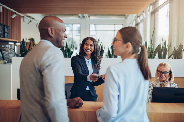 A smiling hotel receptionist helps satisfied guests at the front desk.