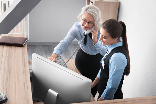 A hotel receptionist shows a new employee how to use the property management system.