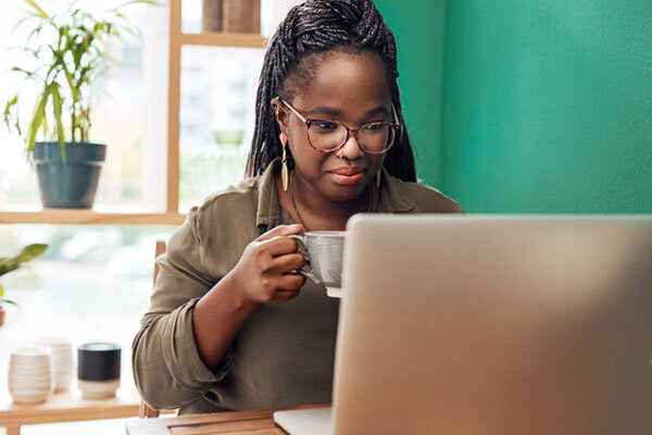 A woman sits at her laptop computer with a hot beverage in her hand, calm and ready to write.
