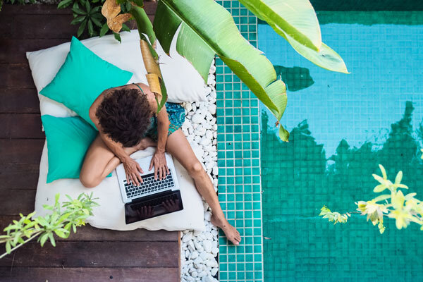 A woman sitting by the pool, working on her laptop.
