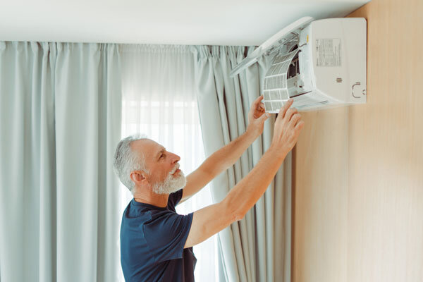 A senior serviceman changes the air conditioner filter in a hotel room.