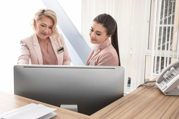 A hotel manager trains a front desk agent on a new property management system.