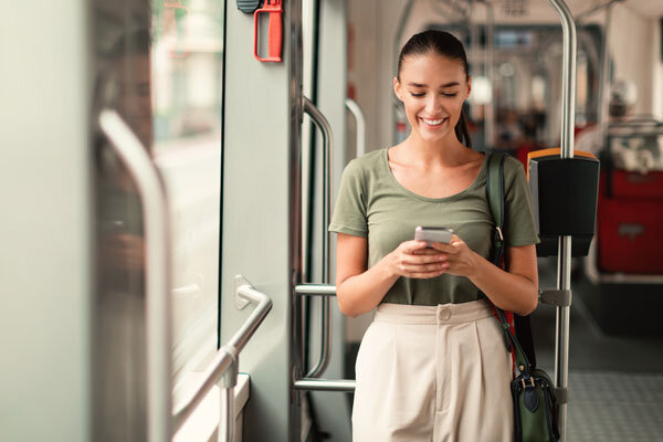 A smiling woman checks out a hotel website on her phone while riding the train home from work and dreaming about her next trip.