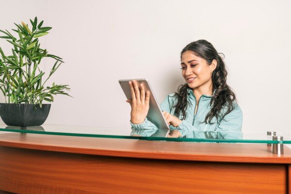 A smiling front desk clerk uses a mobile property management system on a tablet device.