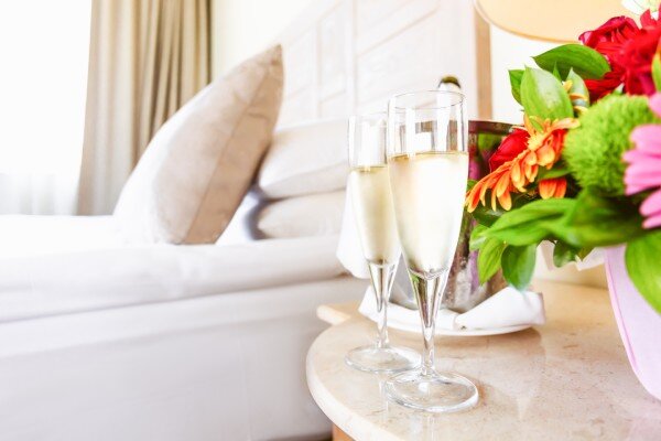 Close-up of upscale hotel bed with a wine cooler and champagne glasses next to it.