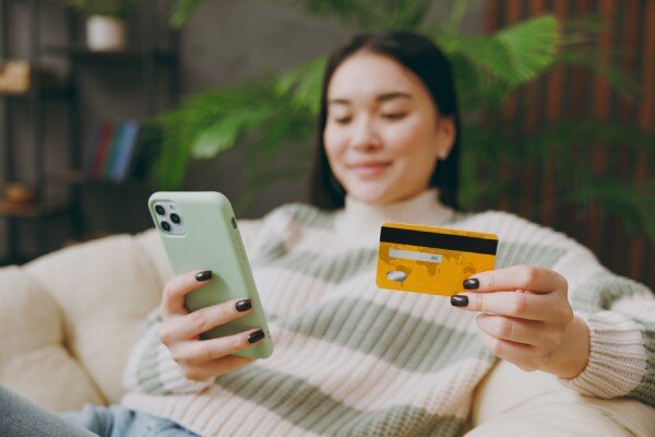 A smiling traveler books a hotel online using their mobile phone, from the comfort of their living room.