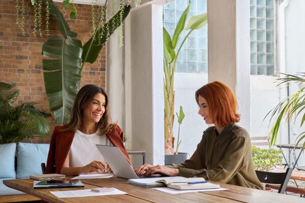 Two woman working together in a pleasant, plant-filled co-working hotel space.