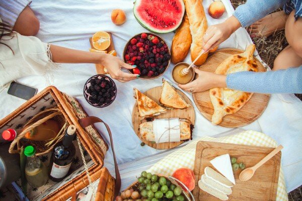 Guests enjoy a prepared picnic of fresh fruit, gourmet cheeses, freshly baked bread, honey, and wine, complete with a wicker basket and a blanket.