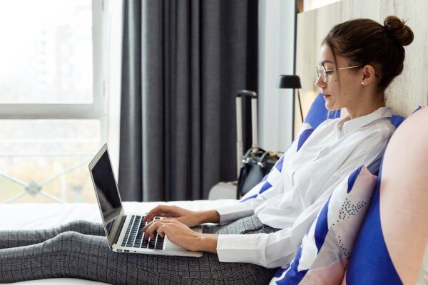 A business traveler working on a laptop from her hotel bed.