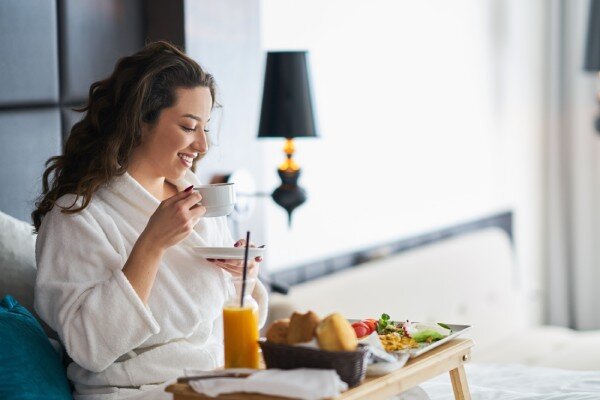 A smiling hotel guest enjoys breakfast in bed.