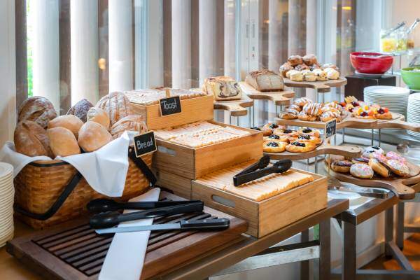 A delicious-looking, well-equipped hotel breakfast station featuring a selection of breads, pastries, and beverages.