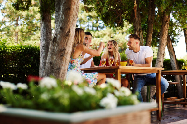 Guests enjoying a drink outside at a table under the shade of a tree.