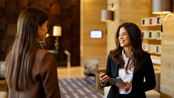 A hotelier equipped with a tablet greets a guest in the lobby.